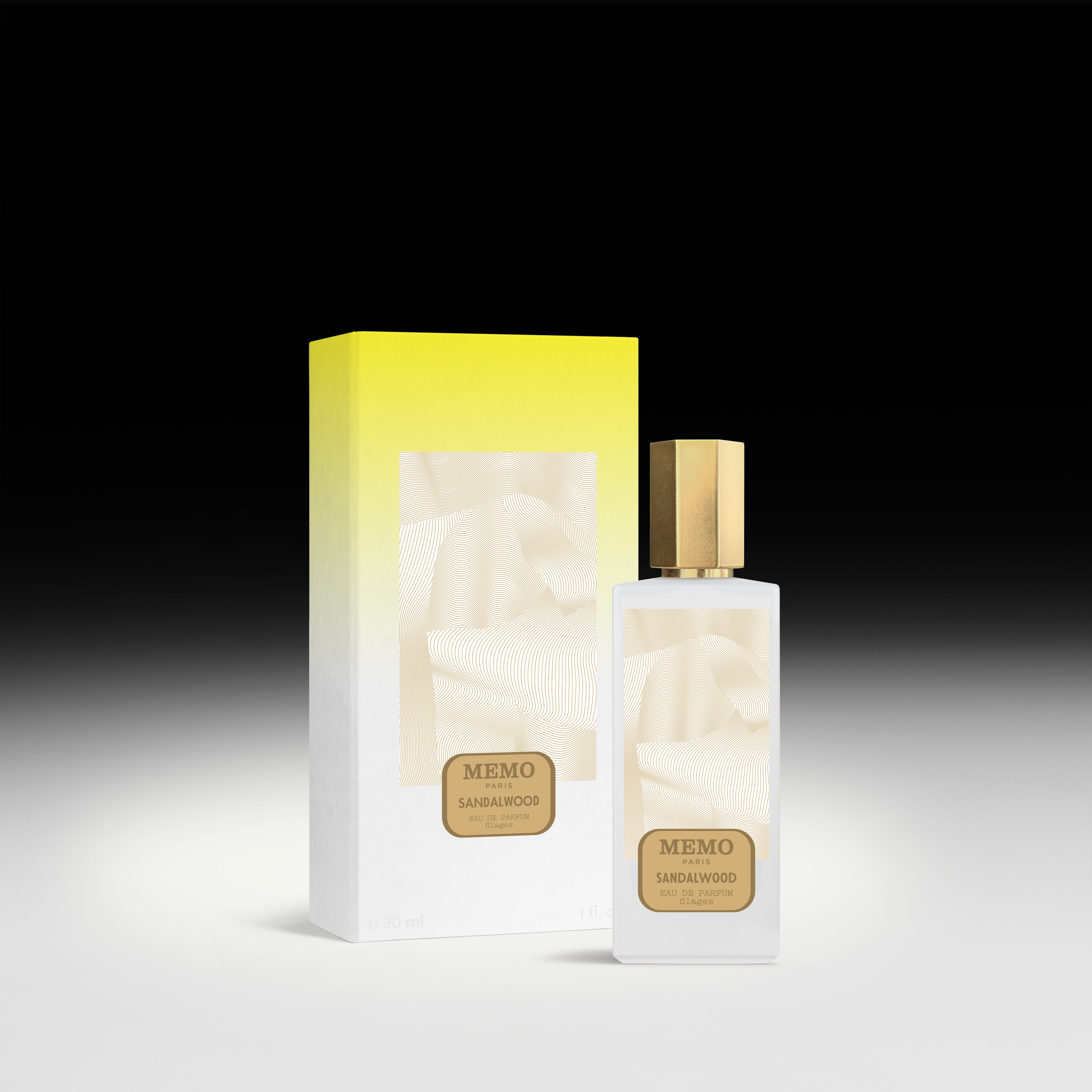 A sleek white glass bottle of memo paris essences filages sandalwood perfume with gold cap beside yellow box