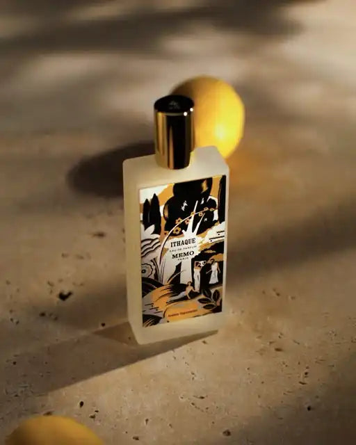 A rectangular frosted glass perfume bottle with a black and gold abstract label and a gold cap.