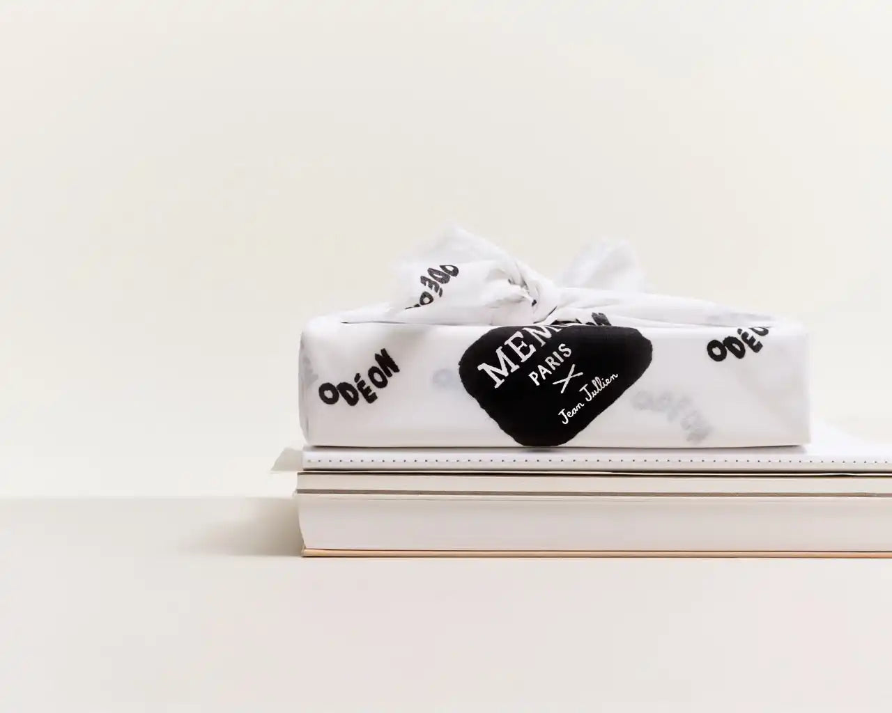 A rectangular gift box wrapped in white paper with black lettering and a black heart-shaped tag.
