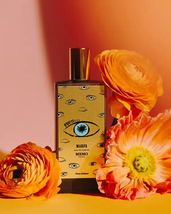 A rectangular glass bottle of perfume with a gold cap and a yellow label featuring an eye motif.