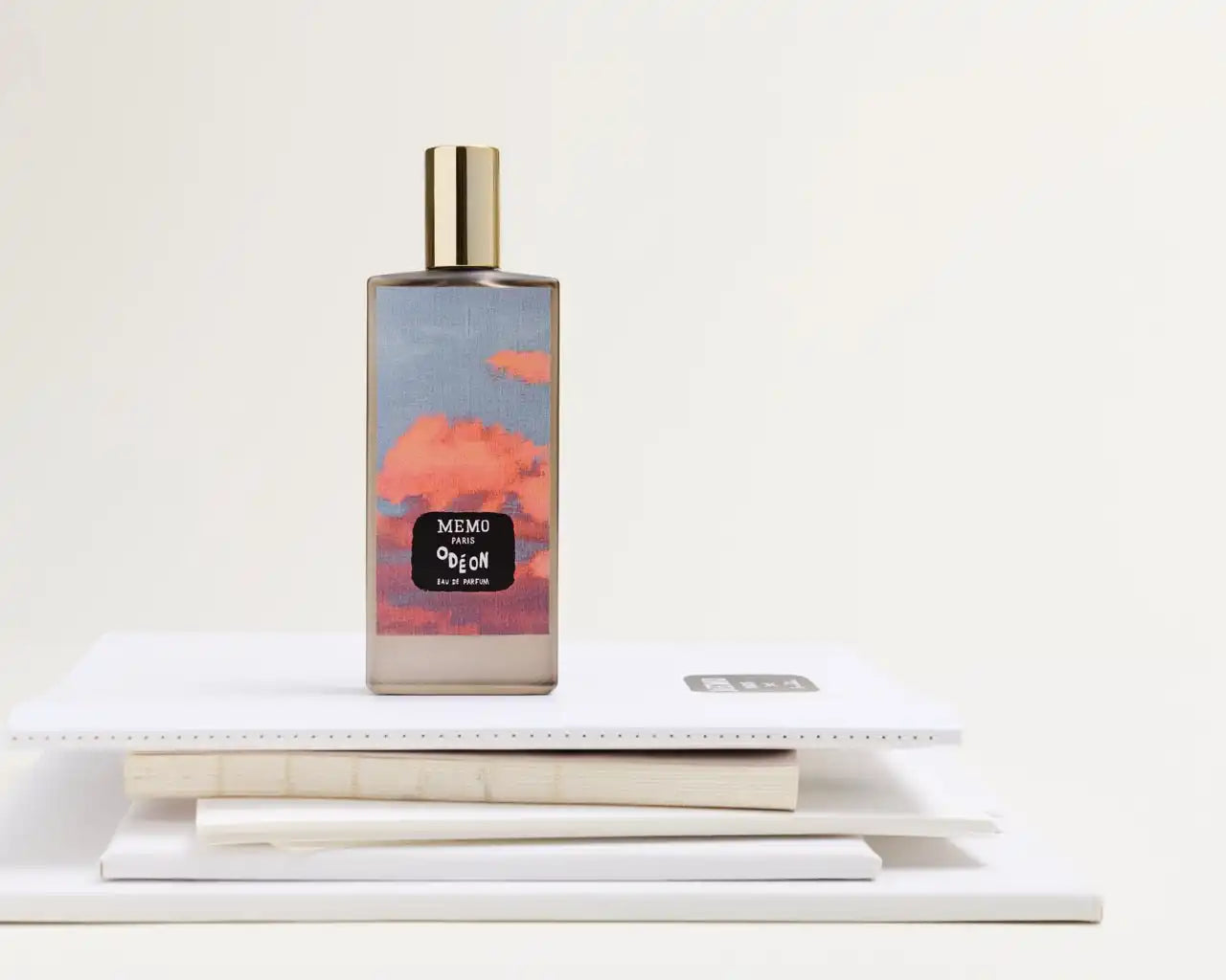 A rectangular glass perfume bottle with a landscape design of pink clouds and a gold cap.
