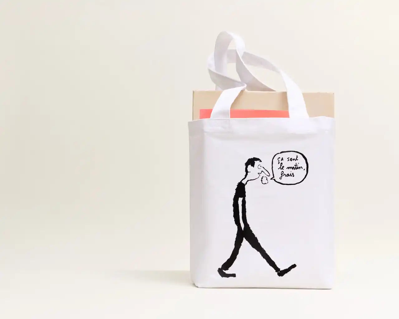 A white canvas tote bag with a black cartoon drawing of a man walking and a speech bubble.