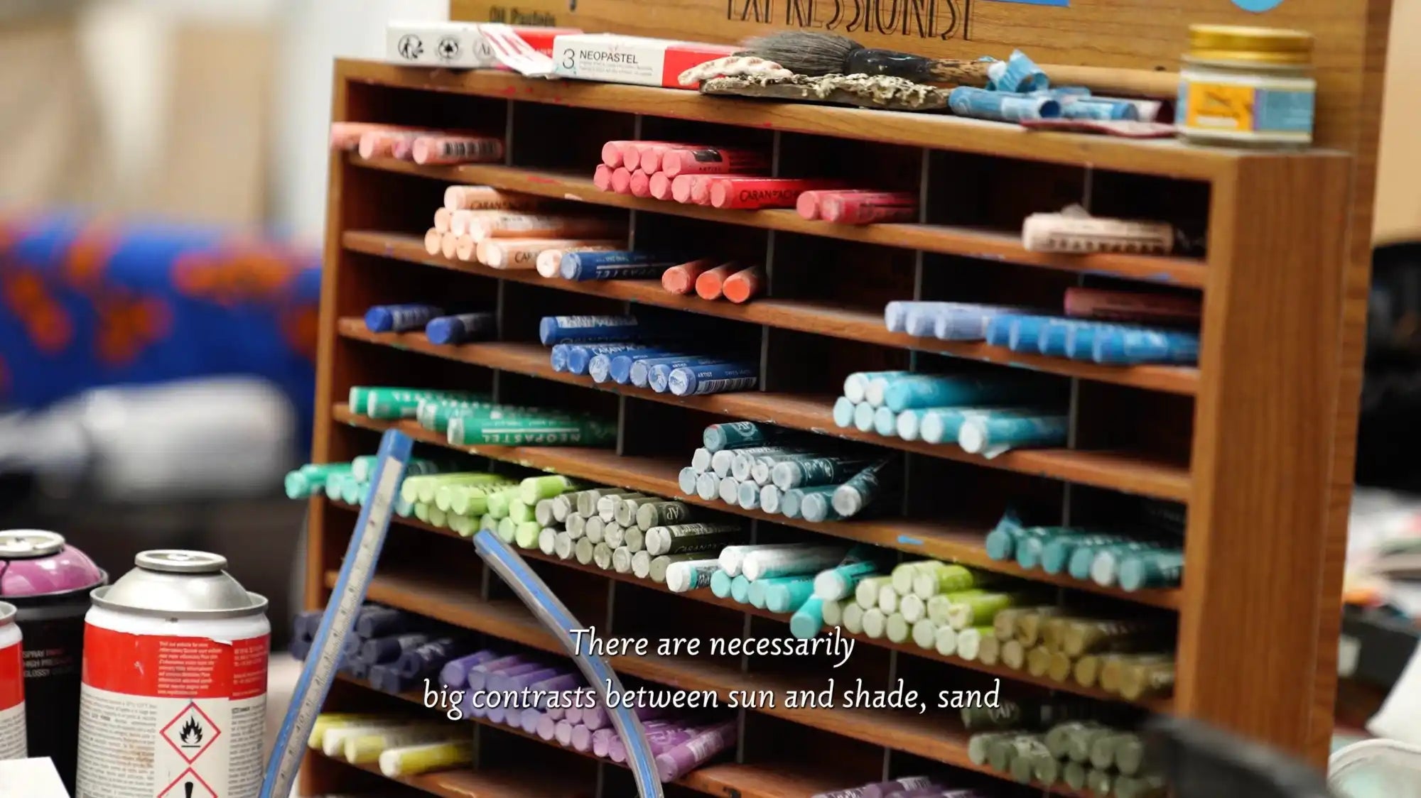A multi-tiered wooden rack filled with rows of colorful art pastels.