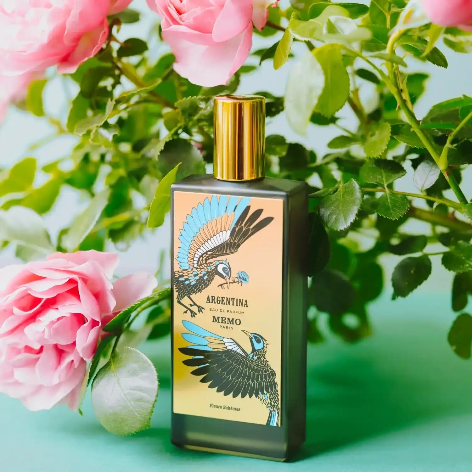 A rectangular black perfume bottle with a golden cap and a colorful label featuring two birds.