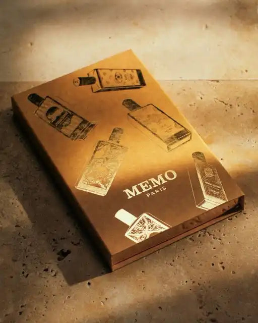 A rectangular, golden-brown box featuring outlines of perfume bottles and ’MEMO PARIS’ text.